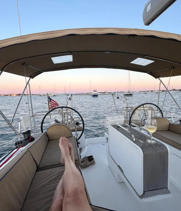 Man's legs propped up on seats facing stern of the boat with sunset in the background 